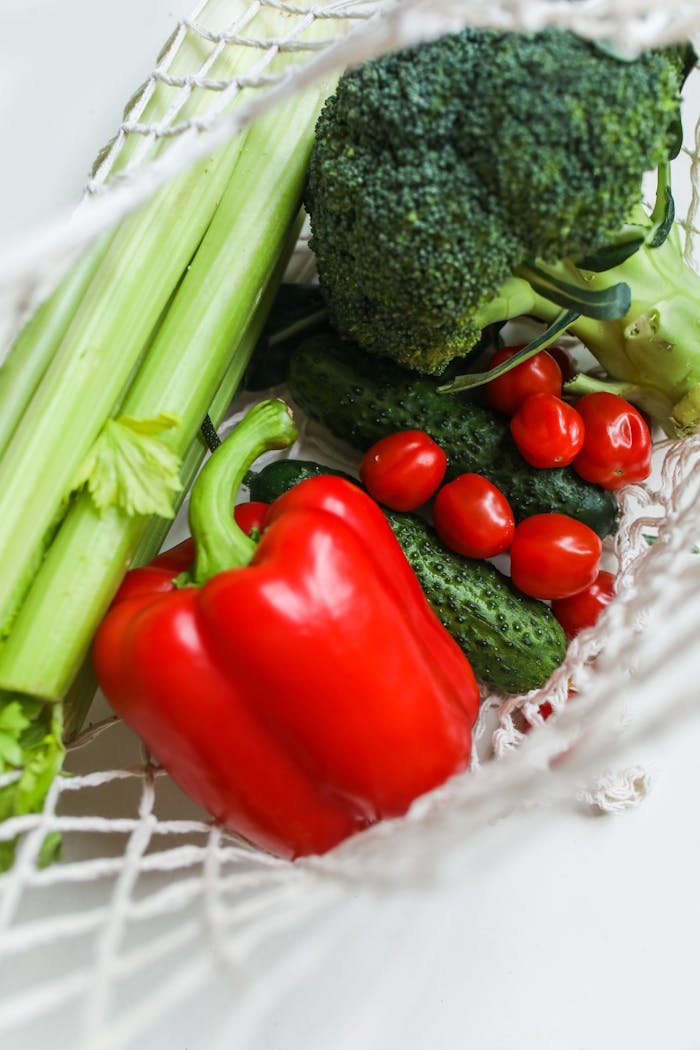 A vibrant mix of fresh vegetables including broccoli, bell peppers, and cucumbers in a net bag.